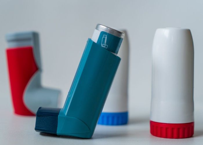 A close-up of various asthma inhalers, including blue, red, and white devices